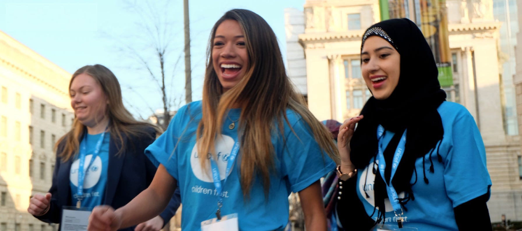 Three young UNICEF volunteers wearing UNICEF blue gather outside a civic building.